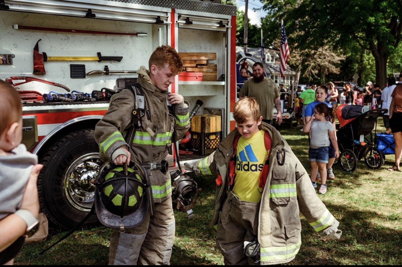 Schaeferville firefighter helping a child try on firefighter turnout gear at a community event